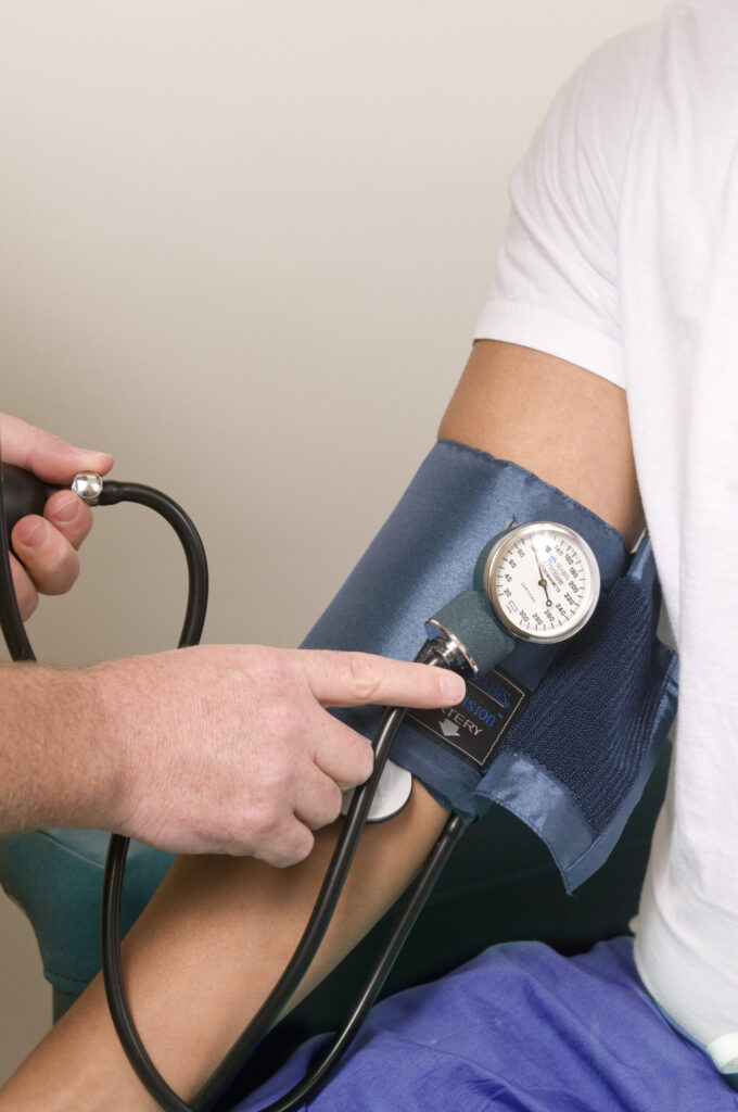 Healthcare worker measuring a seated man's blood pressure with a cuff and stethoscope."
